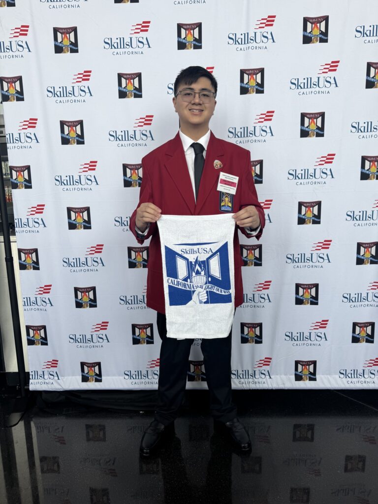 Джей Си на выставке SkillsUSA California держит сине-белый баннер.